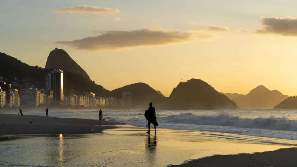 Surfer leaving the beach in Rio de Janeiro at sunset, with Corcovado in the background — one of the best places to visit in Brazil this summer landscape view