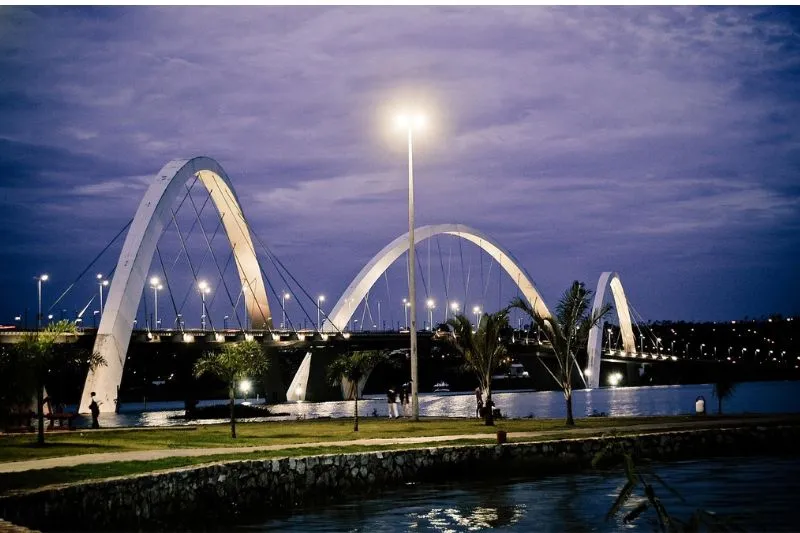 Night view of the Juscelino Kubitschek Bridge arches illuminated over the dark waters of Lake Paranoá in Brasília.
